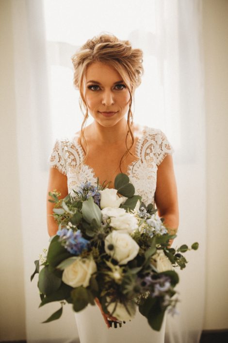 Kaitlin and Carter's Blue and White Pine & Pond Wedding - Bride, Kaitlin, holding her bridal bouquet featuring white Tibet roses, white ranunculus, white astilbe, dusty blue eryngium, light blue delphinium and eucalyptus greenery.