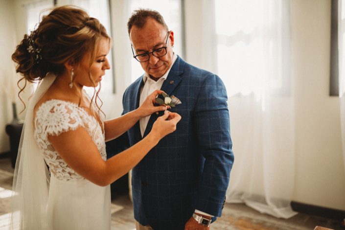 Bride pinning white and blue boutonniere onto Father of the Bride.