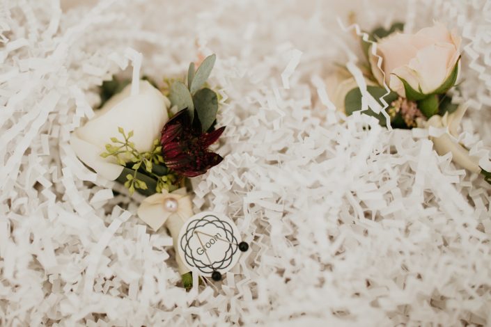 Boutonnieres for Briana and Mark's Glam Jewel Tone Wedding designed with white spray roses, burgundy astrantia and eucalyptus greenery.