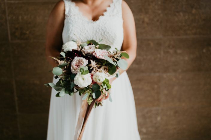 Bride holding jewel tone bridal bouquet designed with dahlias, roses, scabiosa, ranunculus, astilbe and eucalyptus.