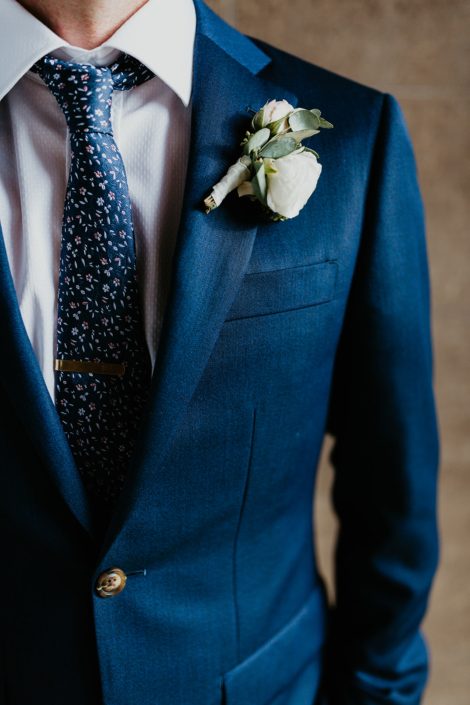 Groom wearing a navy suit and a classic white boutonniere made with spray roses and eucalyptus.