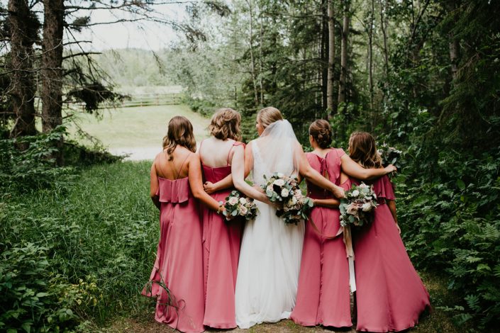 Bride walking with bridesmaids wearing pink berry coloured dresses; holding bouquets designed with burgundy dahlias, white ranunculus, roses, astilbe, scabiosa and eucalyptus greenery.