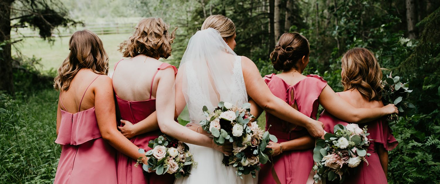 Briana and Mark's Glam Jewel Tone Wedding - Bride and bridesmaids with their backs to the camera holding jewel tone bouquets featuring roses, dahlias, ranunculus, scabiosa, astilbe and eucalyptus greenery.