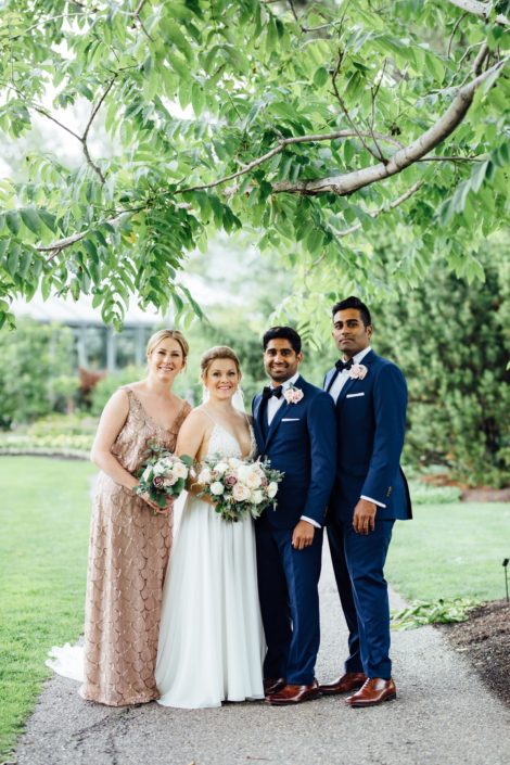 Jill and Jason's Romantic Blush Calgary Zoo Wedding bridal party; groom and groomsmen wearing navy suits and blush spray rose boutonnieres; bride and bridesmaid holding bouquets designed with white o'hara garden roses, quicksand roses, white ranunculus, and light pink astilbe with eucalyptus greenery.