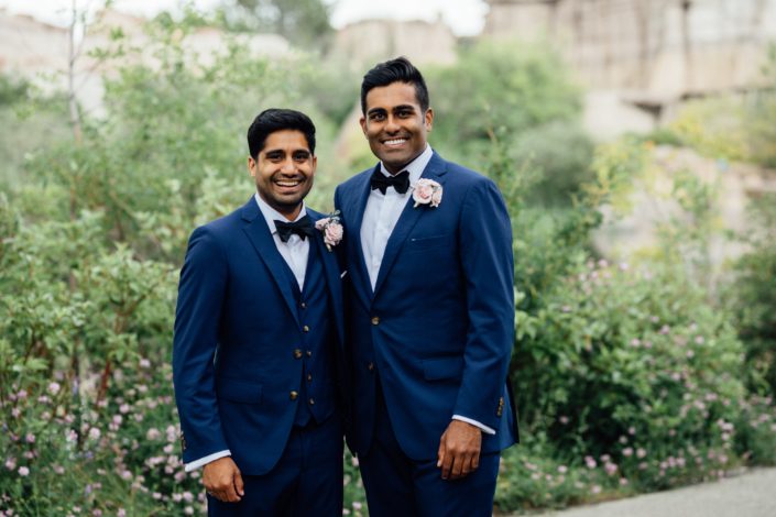 Groom and best man wearing navy suits and blush pink boutonnieres made with spray roses and eucalyptus.
