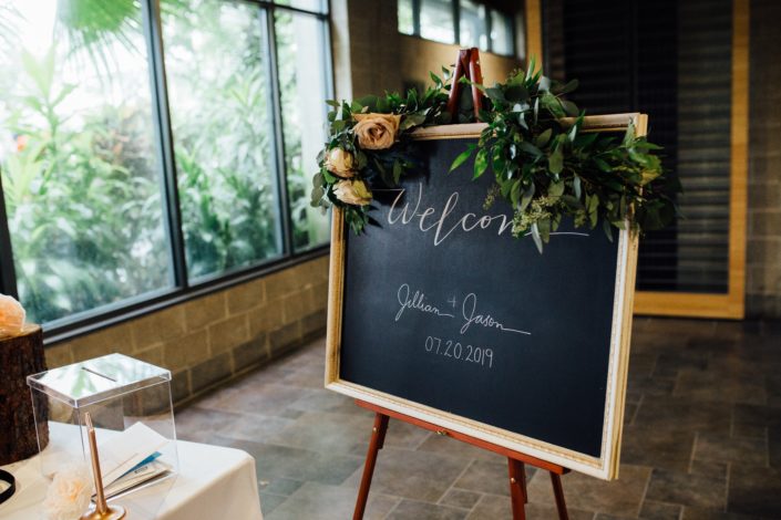 Jill and Jason's Romantic Blush Calgary Zoo Wedding "welcome" sign decorated with a thin fresh greenery garland accented with quicksand roses.