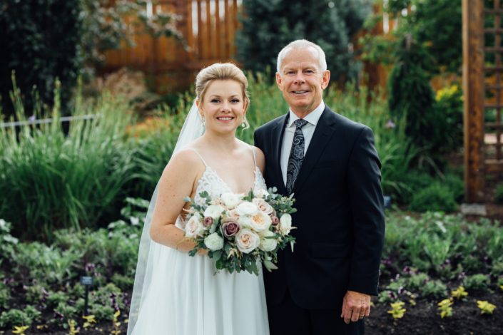 Bride and father standing together with romantic blush bridal bouquet designed with white o'hara garden roses, quicksand roses, white ranunculus, light pink astilbe, and eucalyptus greenery.