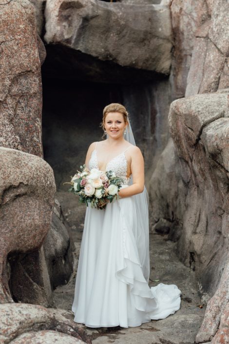 Bride, Jill, at the Calgary Zoo holding romantic blush hand-tied bouquet designed with white o'hara garden roses, quicksand roses, white ranunculus, and light pink astilbe with eucalyptus greenery.