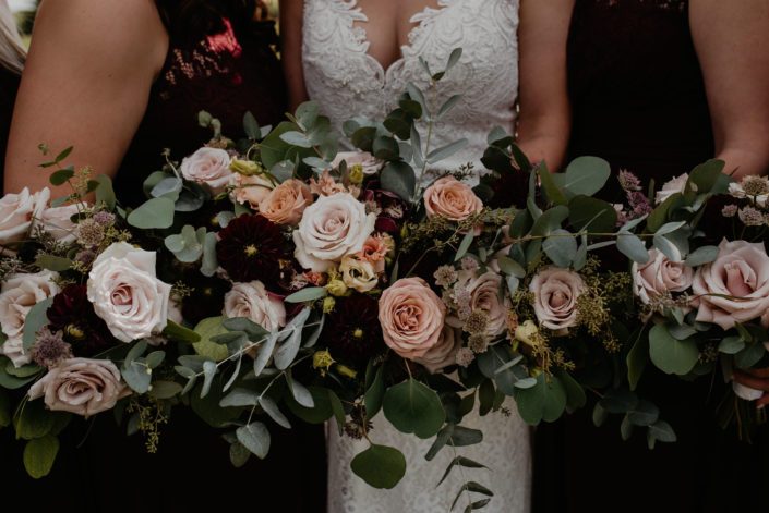 Crystal's bridal bouquet surrounded by bridesmaid's bouquets; designed with burgundy dahlias, quicksand roses, cappuccino roses, peach lisianthus, burgundy cymbidium and pale pink astrantia with eucalyptus greenery.