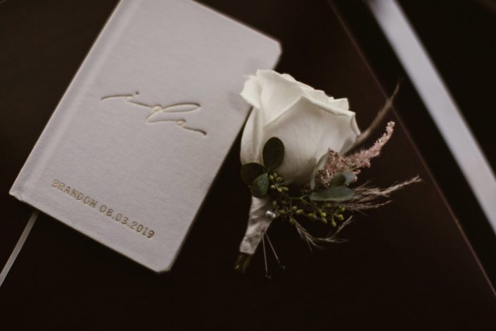 Brandon's white rose boutonniere accented by pale pink astilbe and pampas grass with book of vows.