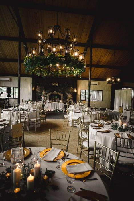 Reception hall at Canyon Ski Resort for Sandra and Brandon's Boho Glam Wedding featuring a greenery garland chandelier arrangement, white linens, and gold accents.