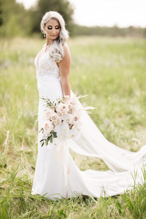 Sandra standing with boho glam bridal bouquet featuring phalenopsis orchids, quicksand roses, pampas grass, olive branches and silver dollar eucalyptus.