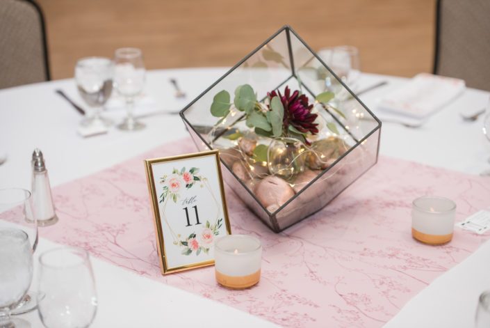 Elegant mauve and ivory wedding centrepieces designed with burgundy dahlia and eucalyptus inside a geometric vase.
