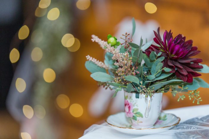 Tea cup filled with pink astilbe and burgundy dahlia with eucalyptus greenery.