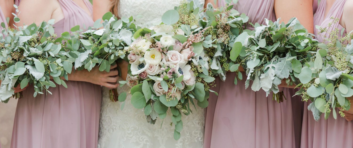 Elegant mauve and ivory bridal bouquet designed with amnesia and quicksand roses, astilbe, ranunculus and panda anemones surrounded by bridesmaids bouquets designed out of eucalyptus and dusty miller greenery accented by pale pink astilbe.