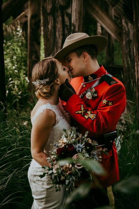 Tanya and Sean's RCMP Wedding - bride and groom kissing with bridal bouquet designed with black baccara roses, burgundy dahlias, navy eryngium, amnesia roses, rose gold succulents, and eucalyptus greenery