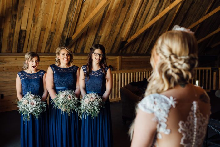 Kelsie's Bridesmaids wearing dark blue dresses and holding bouquets featuring quicksand roses and gypsophila with a variety of eucalyptus greenery.