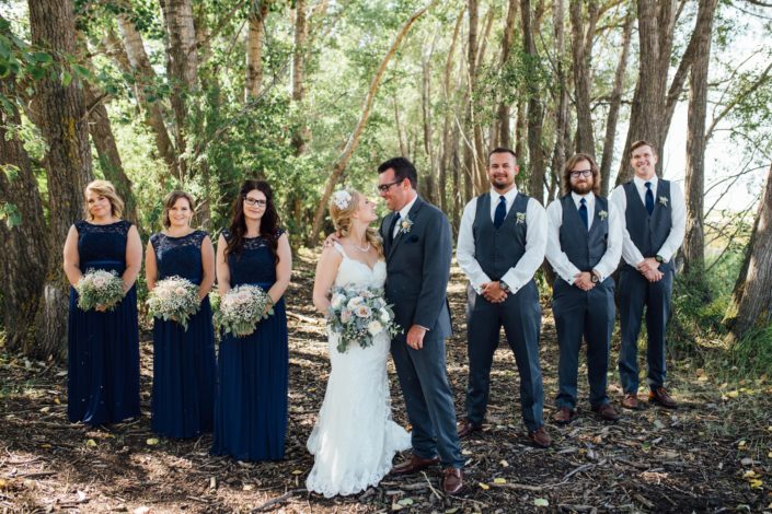 Bridal party for Kelsie and Kyle's Blush and Blue Vintage Barn Wedding - bride holding bouquet designed with blue delphiniums, quicksand roses, white o'hara garden roses, babies breath, succulents and eucalyptus; groom and groomsmen wearing matching boutonnieres, bridesmaids holding bouquets designed with babies breath, quicksand roses and eucalyptus.