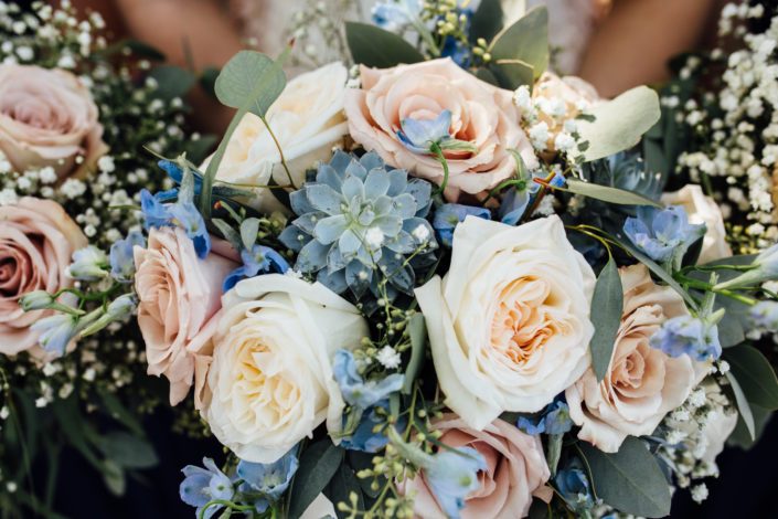 Blush and blue bridal bouquet featuring quicksand roses, white o'hara garden roses, succulents, blue delphiniums, babies breath (gypsophila), and a mixed variety of eucalyptus greenery (feather, gunni, silver dollar and seeded)