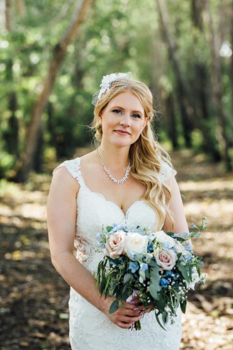 Kelsie wearing a vintage inspired birdcage veil and holding a blush and blue bridal bouquet featuring blue delphiniums, quicksand roses, white o'hara garden roses, succulents, babies breath and eucalyptus greenery.