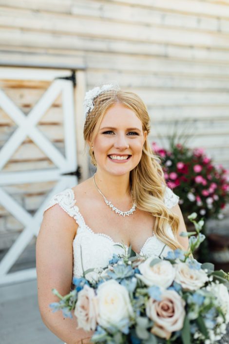 Kelsie holding a blush and blue bridal bouquet designed with succulents, white o'hara garden roses, quicksand roses, blue delphinium, babies breath and a mixed variety of eucalyptus greenery.