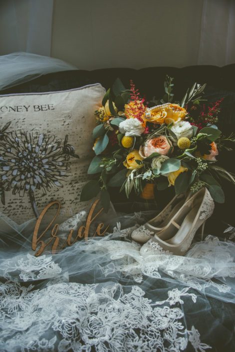 Bride's shoes, veil and mustard yellow bridal bouquet designed with juliet garden roses, caramel antike garden roses, white ranunuclus, golden mustard roses and accented by plum dahlias, craspedia, red astilbe, olive branches and a mixed variety of eucalyptus greenery.