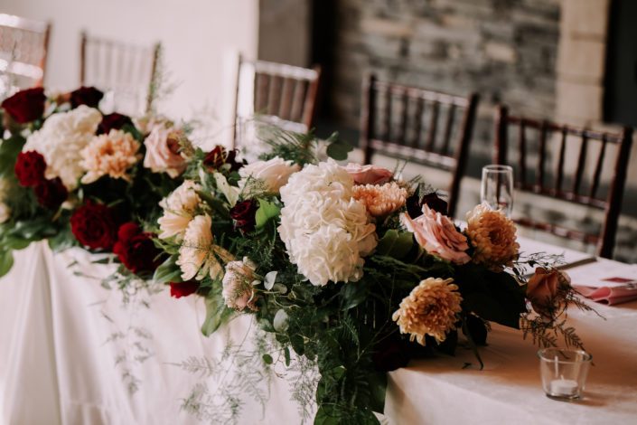 Rustic chic burgundy and blush head table arrangement featuring chrysanthemums, hydrangea and roses.