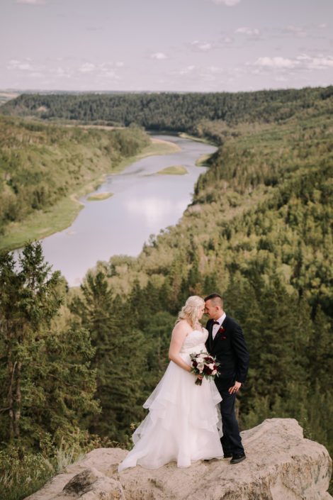 Bride and groom with burgundy and blush bridal bouquet overlooking river valley.