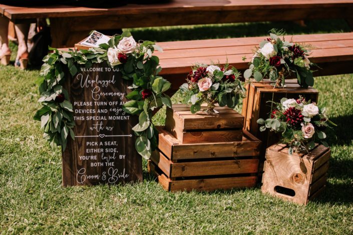 Rustic Chic Burgundy and Blush ceremony decor including fresh arrangements of roses and dahlias in a gold compote vase.