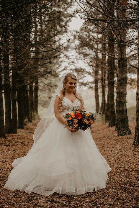 Bride, Haley, with her rustic fall bridal bouquet designed with hearts garden roses, burgundy dahlias, golden mustard yellow roses, orange spray roses, hypericum berries, italian ruscus and seeded eucalyptus.