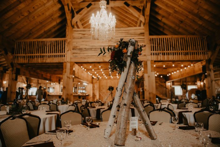 Teepee centrepiece for Hayley and James' rustic fall wedding designed with burgundy dahlias, hearts garden roses, orange spray roses and solidago with seeded eucalyptus and italian ruscus greenery atop a teepee of birch poles.