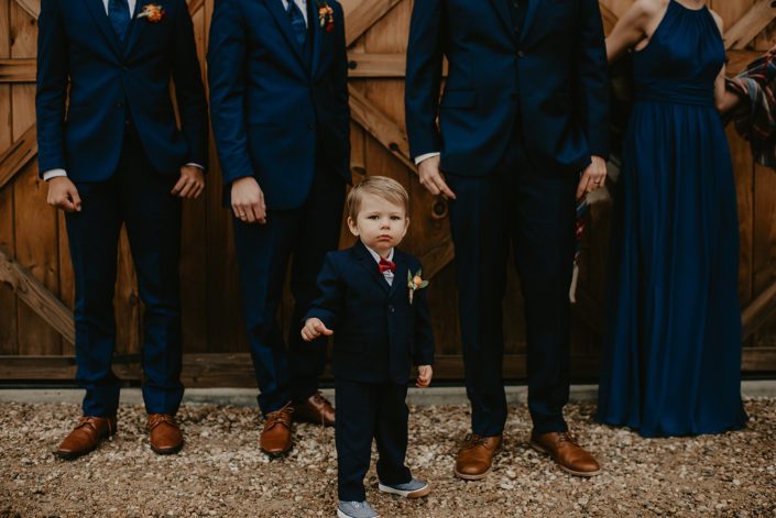 Rustic Fall Wedding ring bearer wearing a magnet boutonniere designed with orange spray roses, hypericum and greenery.