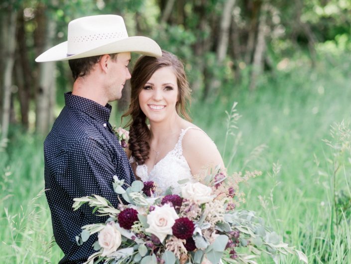 Bride and cowboy with burgundy country chic bridal bouquet featuring dahlias, lisianthus, quicksand roses, astrantia, astilbe, dusty miller, eucalyptus and olive branches