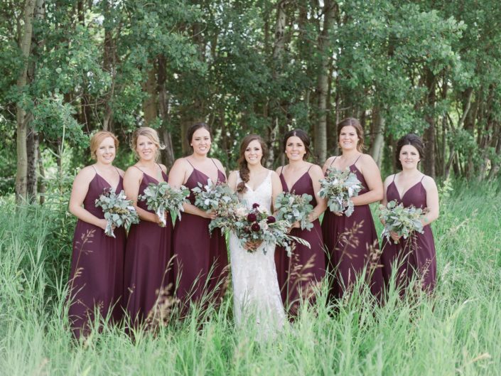 Burgundy country chic wedding bride and bridesmaids holding bouquets; bridal bouquet designed with dahlias, quicksand roses, lisianthus, astrantia, astilbe and various types of greenery including eucalyptus, dusty miller and olive branches; bridesmaids carrying greenery bouquets.