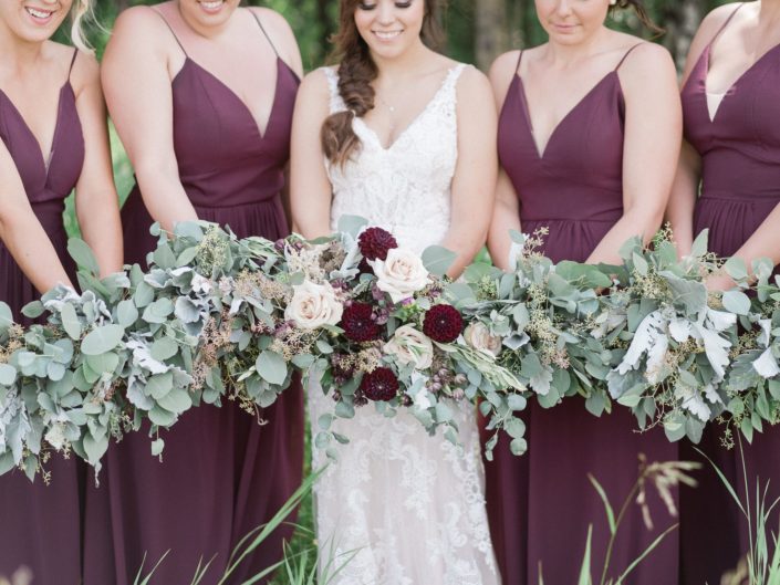 Bride, Santaya, and bridesmaids bouquets; bridesmaids carrying greenery bouquets designed with dusty miller, eucalyptus and olive branches; bridal bouquet designed with quicksand roses, burgundy dahlias, astilbe, astrantia, brown lisianthus and matching greenery.