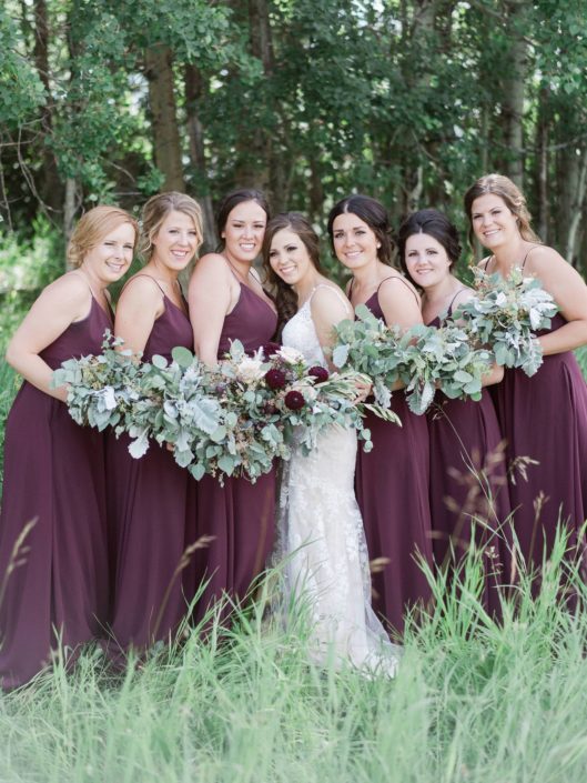 Bride and bridesmaids wearing burgundy and carrying greenery bouquets; bridal bouquet has a burgundy country chic feel and featured dahlias, quicksand roses, olive branches, dusty miller and seeded eucalyptus.