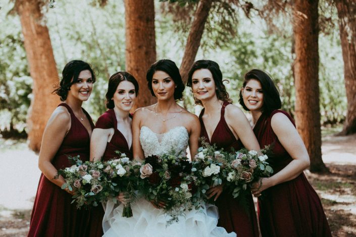 Bride and bridesmaids; wearing burgundy dresses and carrying bouquets designed with dahlias, garden roses, roses, lisianthus, plumosa and eucalyptus