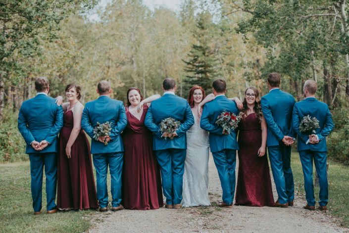 Hailey and Brandon's bridal party; bride and bridesmaids facing camera, groom and groomsmen holding bouquets with backs to camera