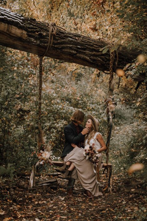 Down the aisle fall styled shoot - Couple in the woods on a swing with neutral fall flowers