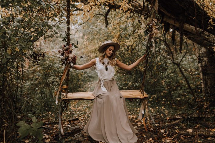 Boho girl swinging on a flower covered swing in the woods