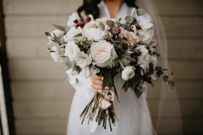 Brittany's bridal bouquet designed with white o'hara garden roses, quicksand roses, white ranunculus, white lisianthus, burgundy astrantia and eucalyptus greenery with rose gold photo locket