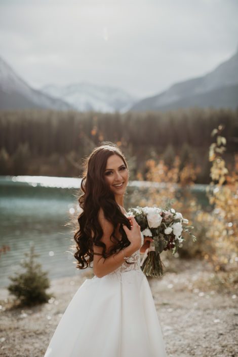 Brittany standing in front of a lake in the Rocky Mountains with her blush and ivory bridal bouquet