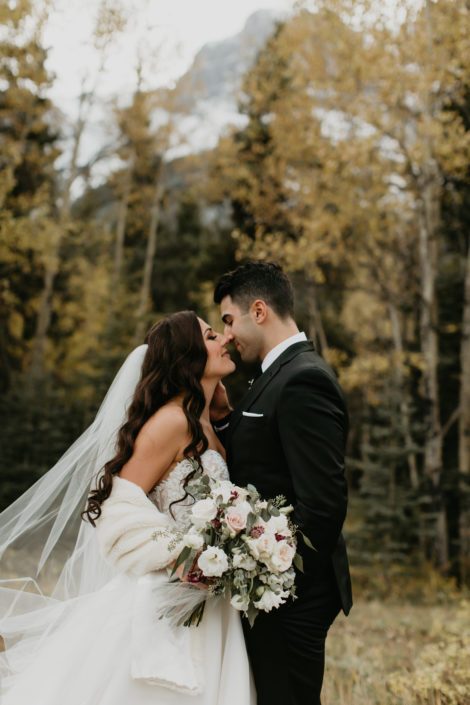 Elegant Canmore Wedding - Brittany and Briggs almost kissing with blush and ivory bridal bouquet made of burgundy astrantia, quicksand roses, white o'hara garden roses, lisianthus, ranunculus and eucalyptus