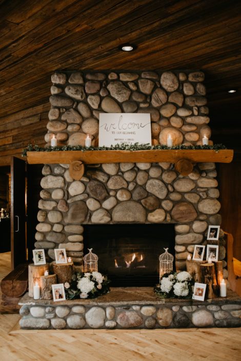 stone fireplace decorated with candles, photo frames, greenery and flower arrangements featuring white hydrangeas