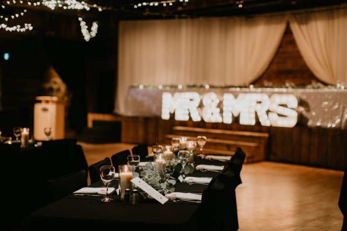 Reception tables decorated with candles, eucalyptus and babies breath with black table cloths and white napkins