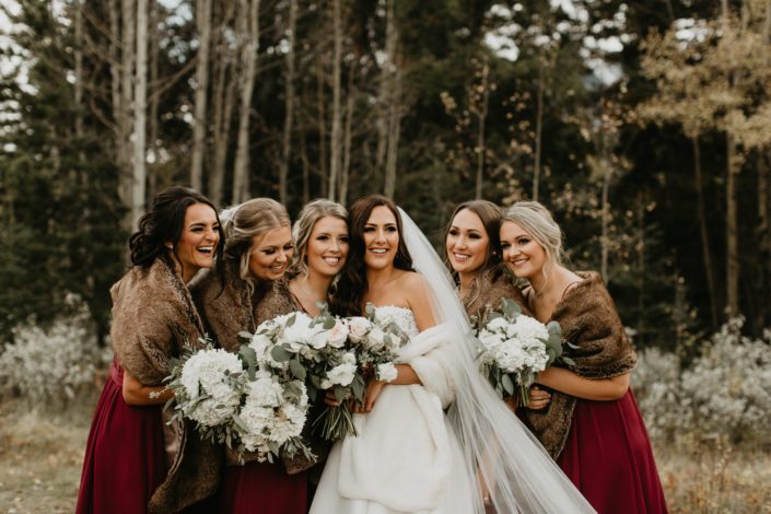 Brittany and her bridesmaids wearing fur shawls and holding white bouquets; bridesmaids bouquets were designed with hydrangeas and eucalyptus; bride's bouquet designed with white o'hara garden roses, quicksand roses, white ranunculus, lisianthus, burgundy astrantia and eucalyptus greenery