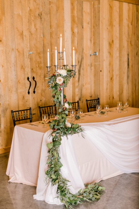 Winter wedding blush and burgundy flower garland climbing up tall candlestick holder