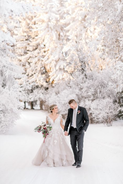Bride and groom walking in a snowy winter wonderland with blush and burgundy bridal bouquet; blush and burgundy winter photoshoot