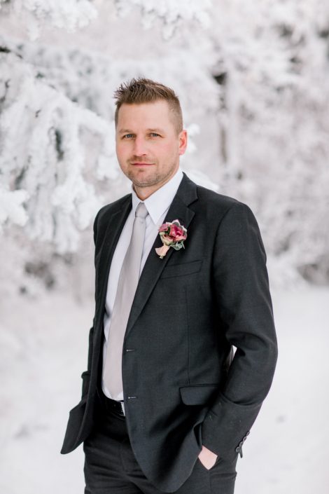Winter groom standing in snow wearing blush and burgundy boutonniere
