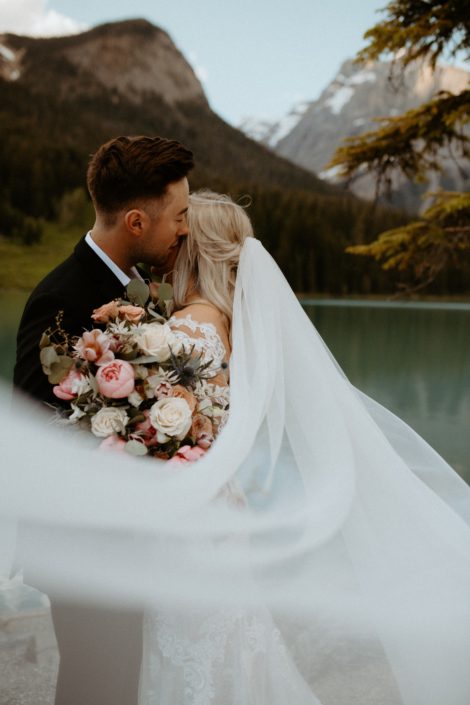 Bride and groom with windswept veil and pink and white bridal bouquet featuring peonies, roses, tulips and eryngium with eucalyptus greenery